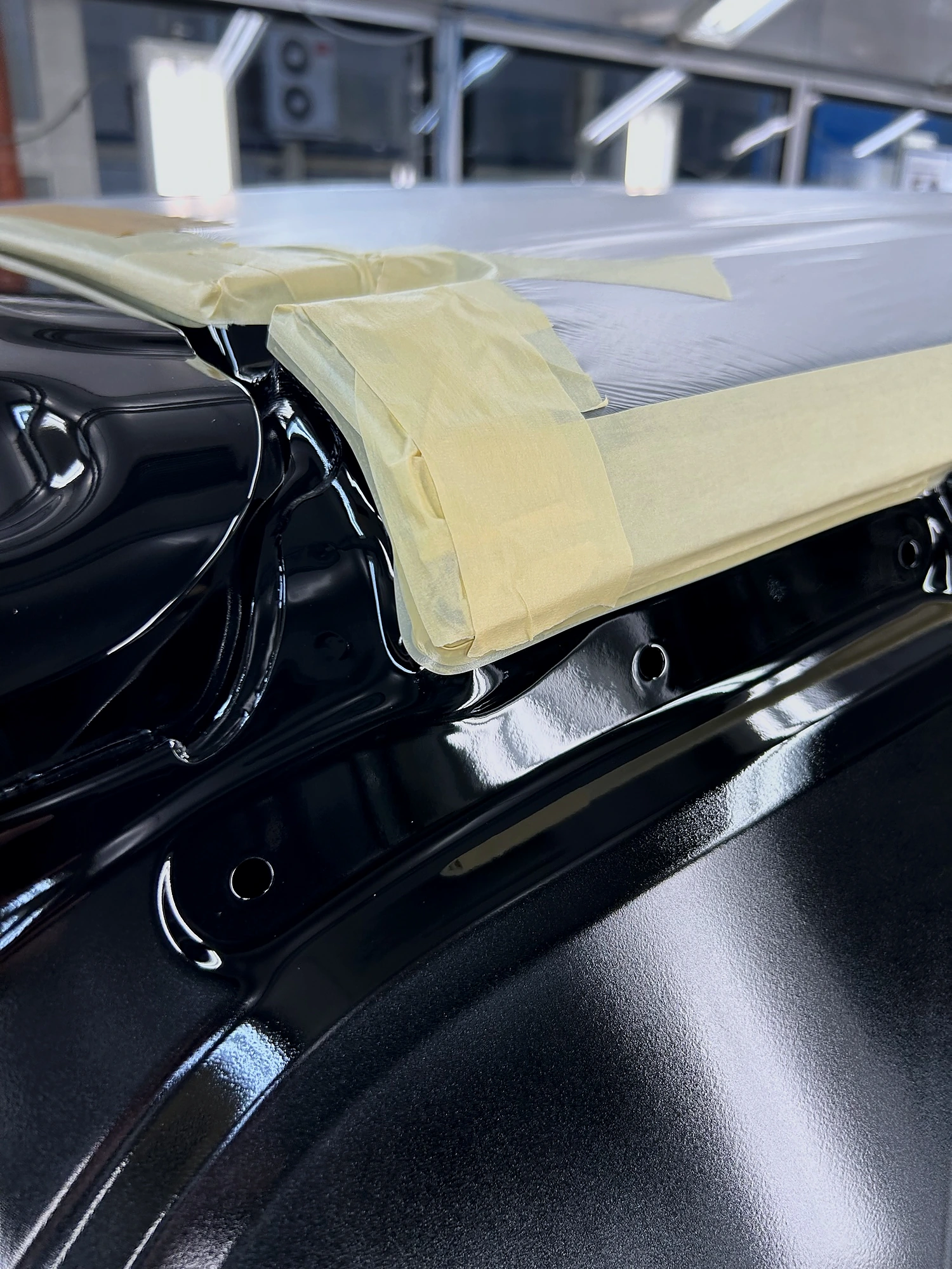 Masking tape applied along a freshly painted black car body on the line